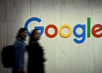 Google logo on building wall with blurred pedestrians walking past