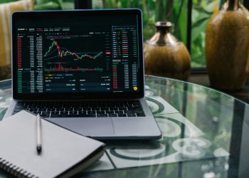 Laptop screen showing fluctuating tech stock charts with notebook on desk